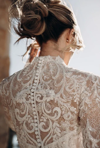 Bride wearing lace wedding dress with long sleeves, high neckline and fabric covered buttons