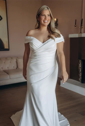 Plus size bride wearing simple wedding gown with draping and off the shoulder straps